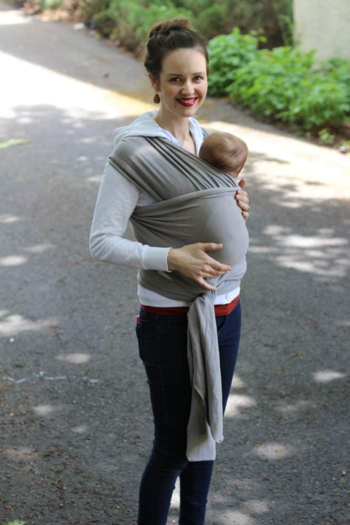 Newborn baby inside of a grey Boba wrap outside on a sunny day