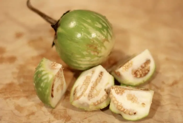 green thai eggplant sliced into 4 pieces on a cutting board for thai curry