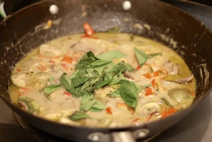 fresh thai basil tossed on the top of cooked green curry in a cast iron pan