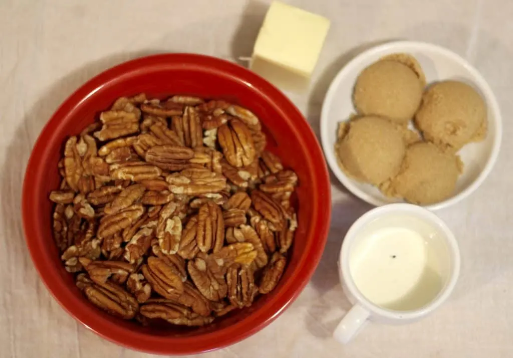 A red fiestaware bowl with pecans, with other white bowls filled with brown sugar, butter, and cream for making candied pecans