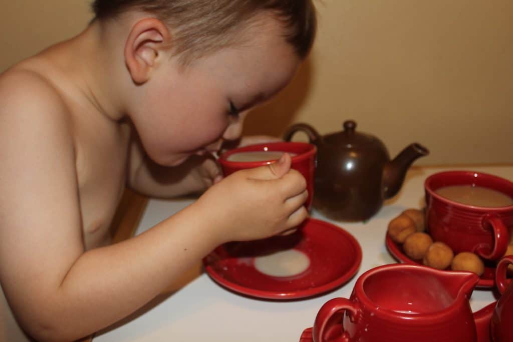 Indoor activities with a toddler like this toddler boy drinking tea out of red scarlet fiestaware