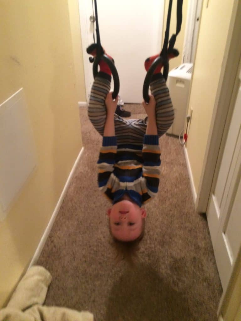 toddler boy swinging in a hallway upside down on gymnastics rings; indoor activities for toddlers