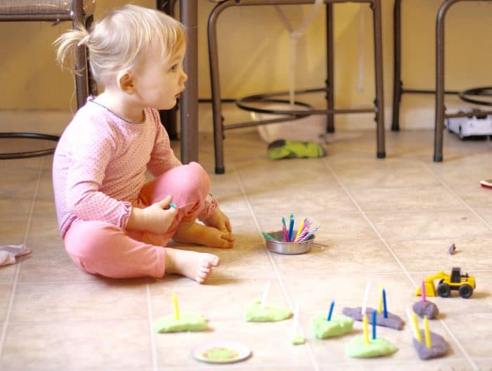 Toddler girl playing Play Doh on the floor with birthday candles, a perfect indoor activity for toddlers