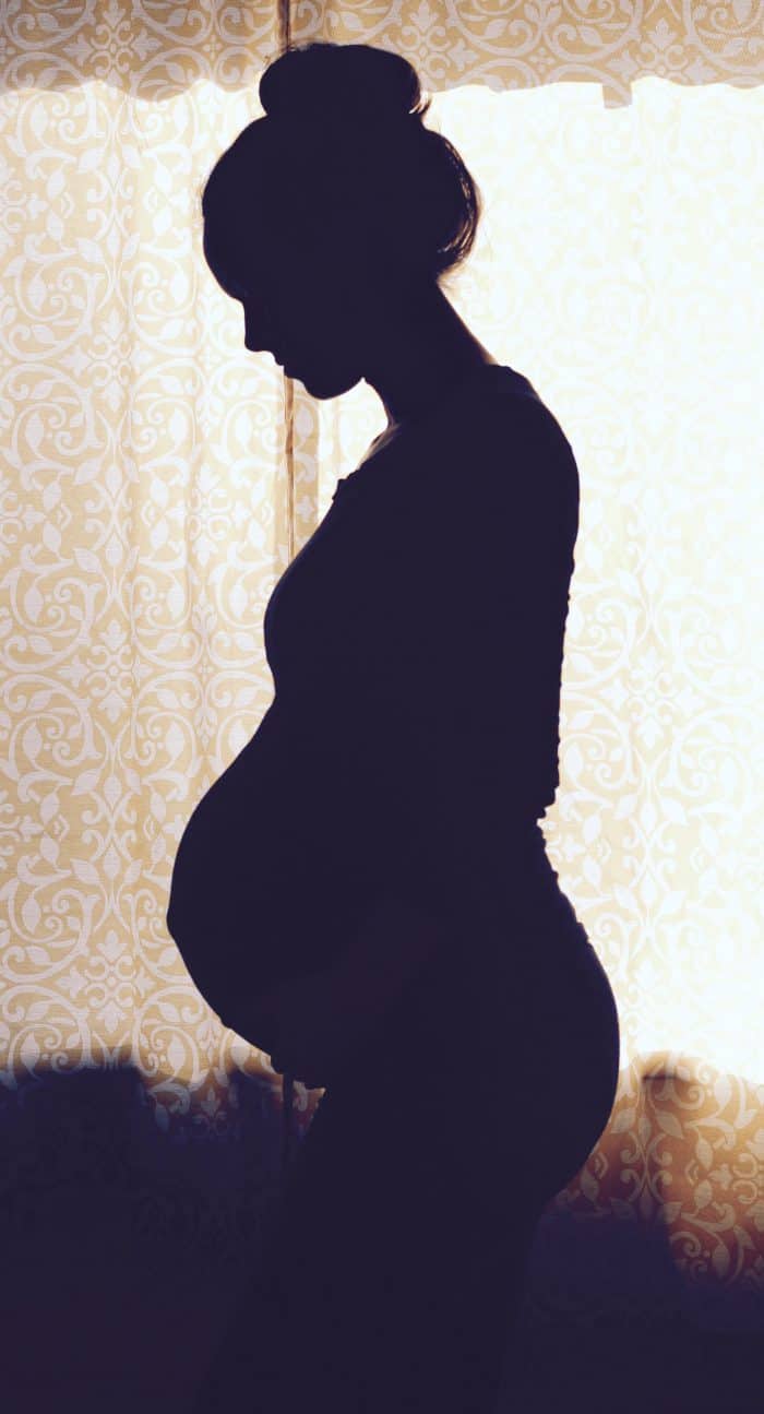 Edited photo of a pregnant woman in a bun taking her own pregnancy silhouette photo around 8 months pregnant