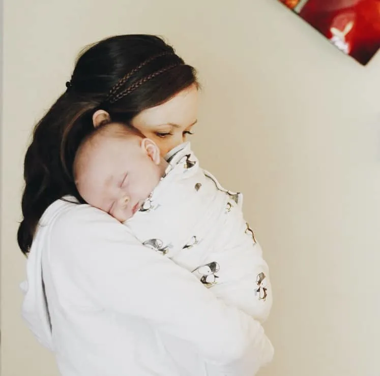 a mom holding her newborn baby swaddled