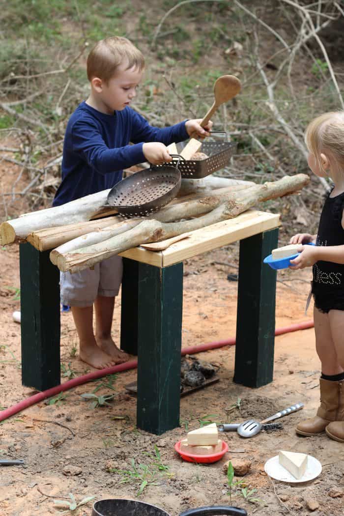 two kids playing outside making pretend food on a wooden diy outdoor play kitchen