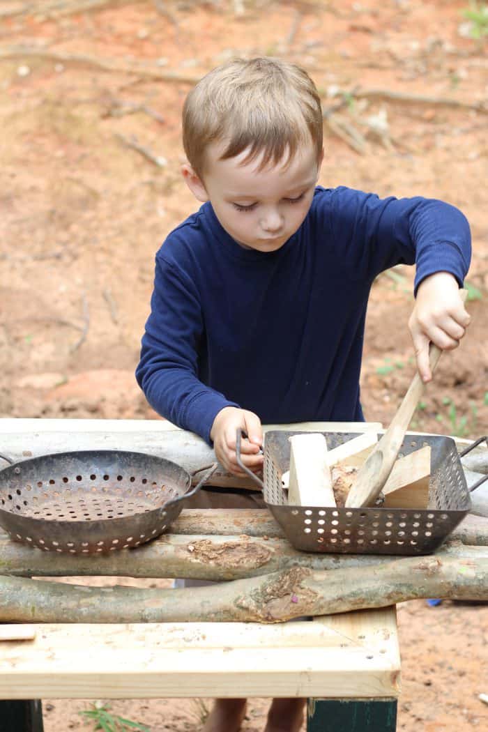 a boy stirring wooden blocks in a diy outdoor play kitchen 