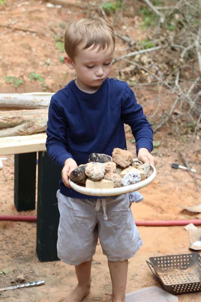 A toddler boy carrying rocks on a frisbee