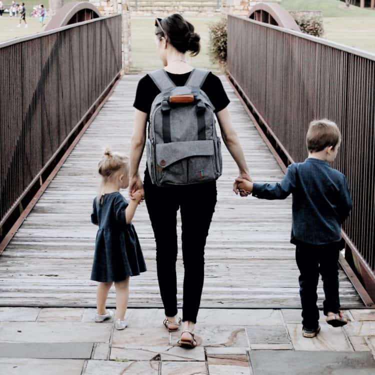 how to be less busy as a mom: a mom walking over a bridge with her daughter and son holding hands