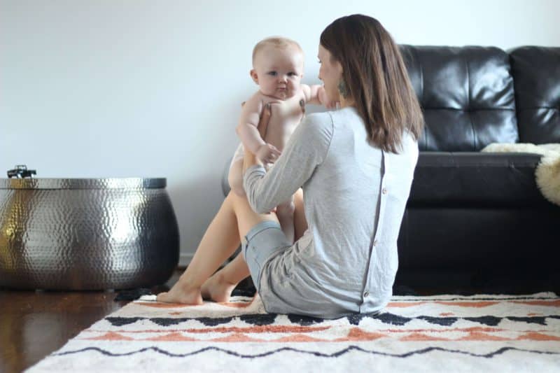 a mom holding her baby on the floor next to a leather couch and orange azteca terracota lorena canals rug