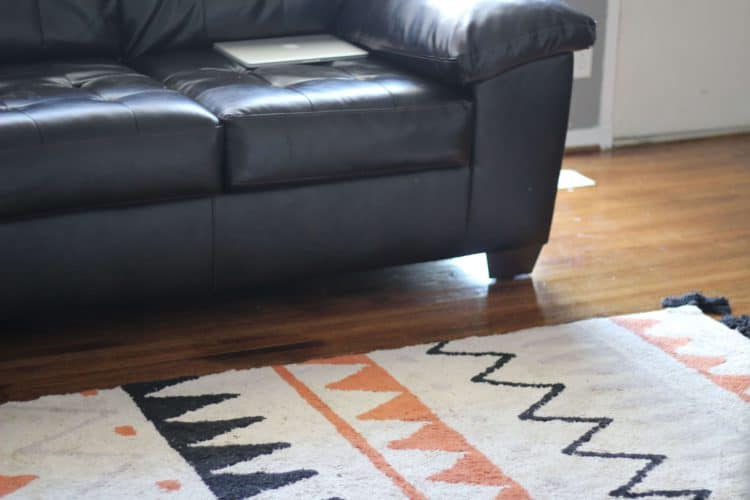 lorena canals rug in black and orange terracota next to a brown leather couch