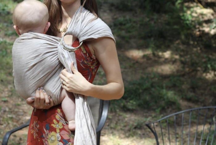 A mother holding her bald baby in a Lillebaby ring sling colored golden harvest