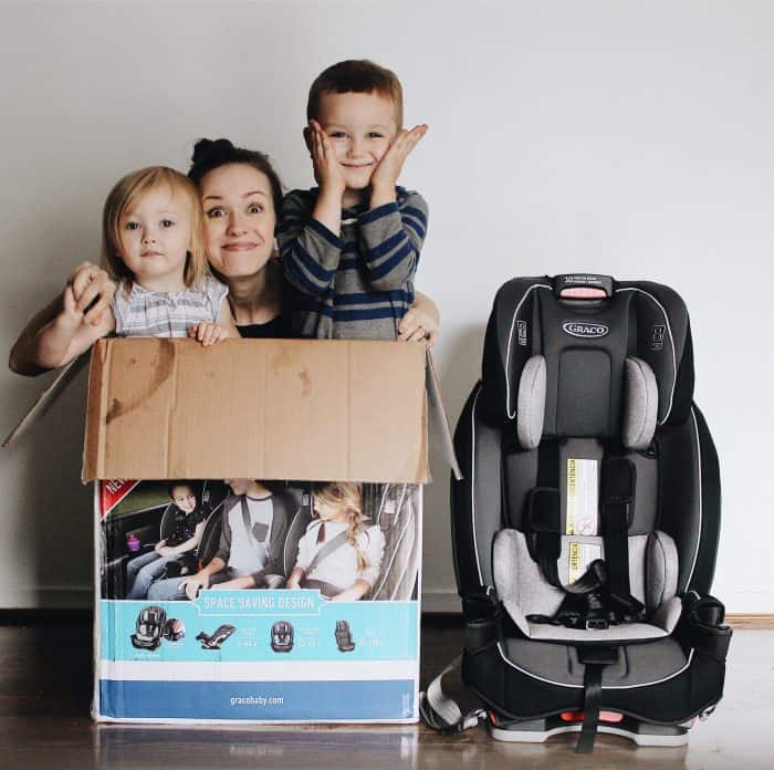 mom and her two kids inside of a box smiling, which is next to a black graco slim fit car seat