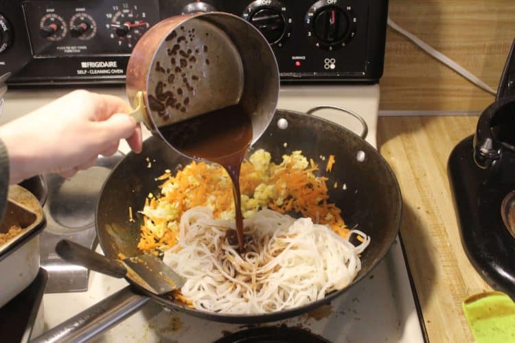 adding pad thai sauce to noodles