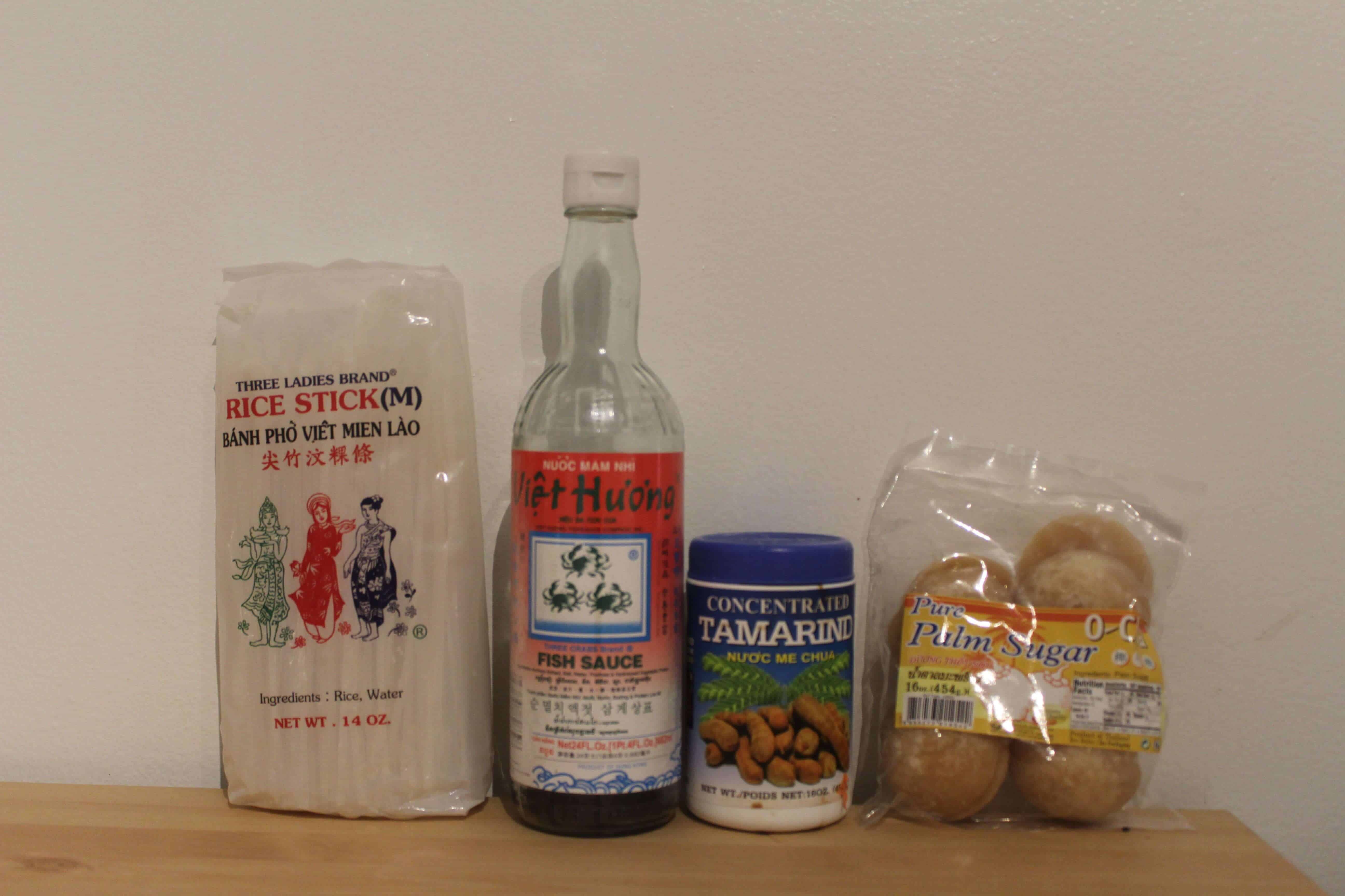 rice noodles, 3 crabs fish sauce, tamarind paste, and palm sugar on a table ready to make vegetarian pad thai sauce