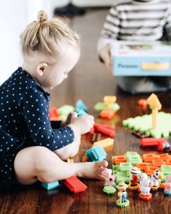 A preschool girl playing with Picasso Tiles 100 piece Bristle Shape Blocks 