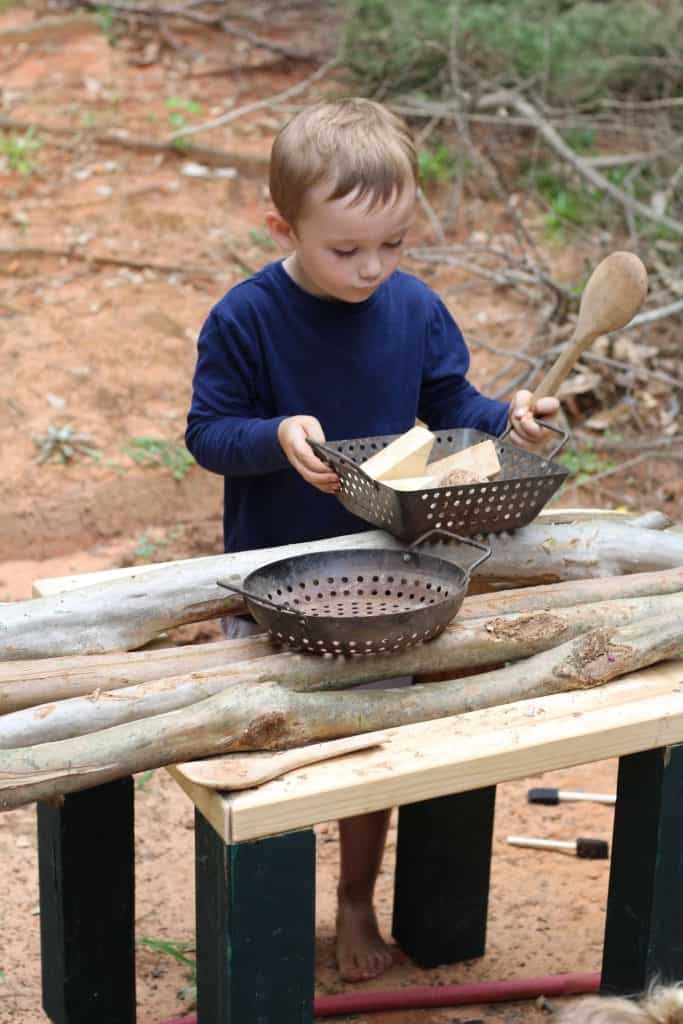 preschool boy playing outside in an outdoor play kitchen, part of a homeschool preschool 