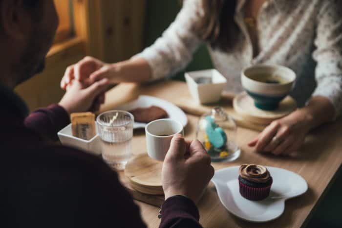 a couple holding hands as they hold coffee mugs at a restaurant