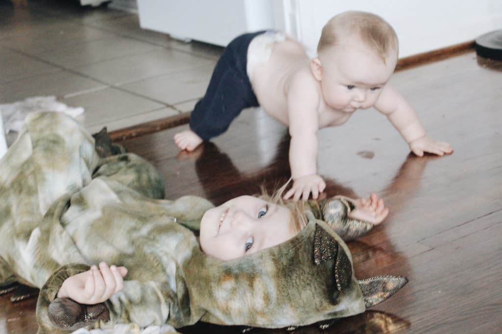 a toddler playing dress up in a green dinosaur costume