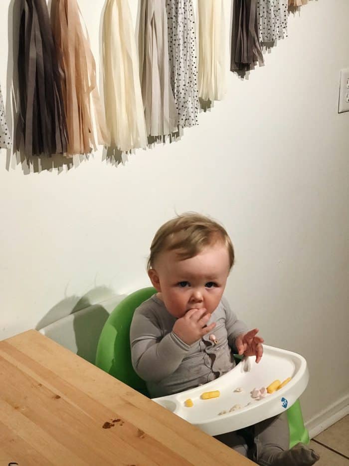 a baby picking up baby led weaning foods from his highchair and bringing them to his mouth