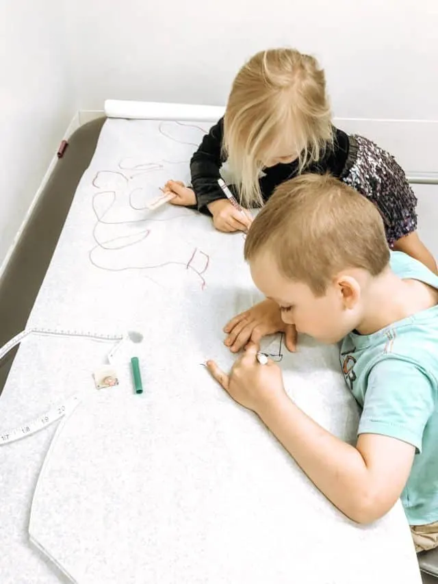 a 3 and 5 year old coloring with markers on the doctor's table waiting for the nurse to arrive.