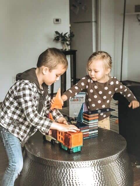 Picasso tiles 180 piece magnetic tile set being played with by two kids on a shiny metal table. 