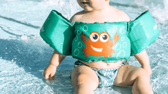 Toddler sitting in water wearing a green puddle jumper and swim diaper.
