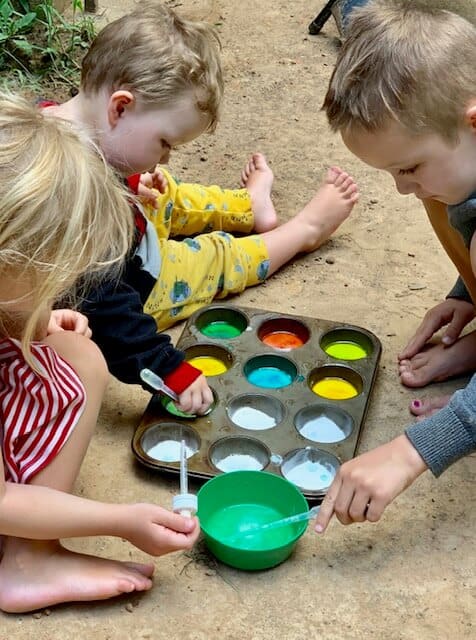 Kids doing Busy Toddler's Playing Preschool Year 1 Activity adding vinegar to baking soda and food coloring in a muffin tin. 