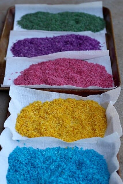 Blue, yellow, pink, and purple dyed rice on paper towels drying for sensory bin play. 