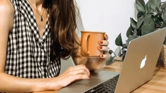 a woman holding a coffee mug while working on a mac computer