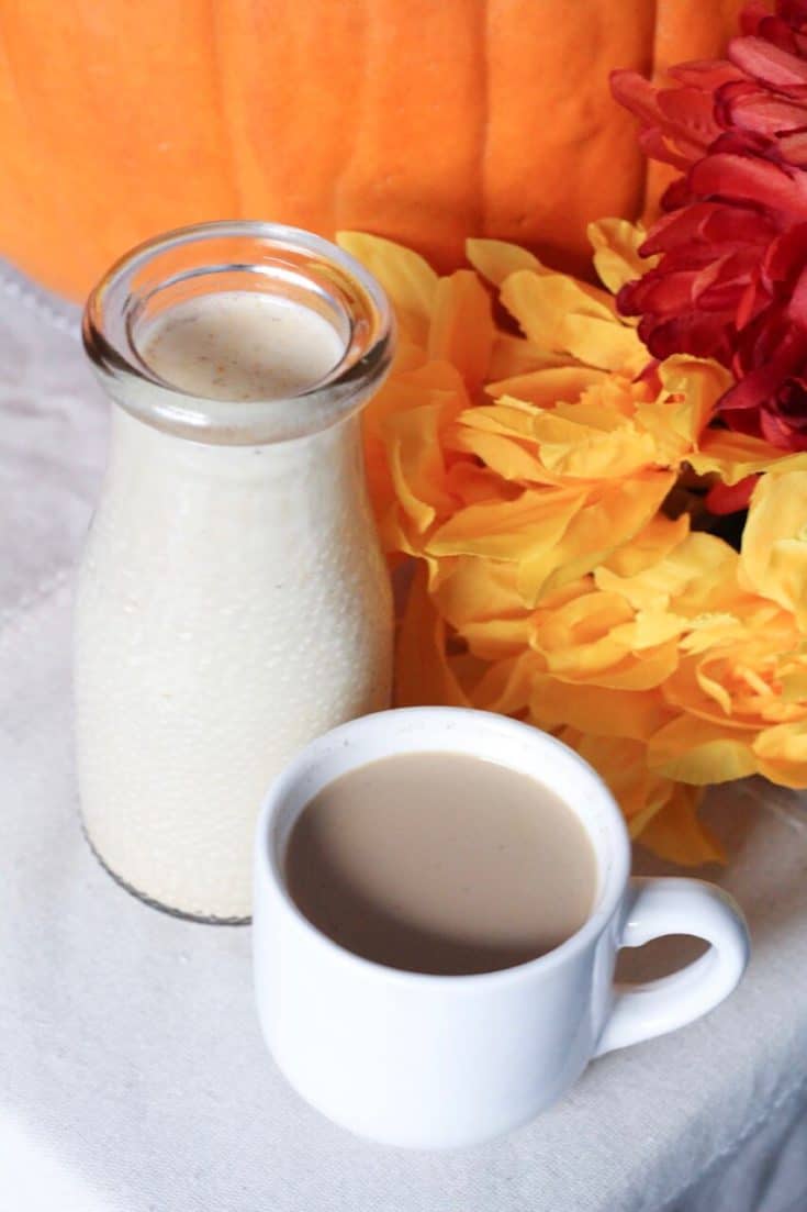 homemade pumpkin spice coffee creamer in a carafe next to a pumpkin and cup of coffee