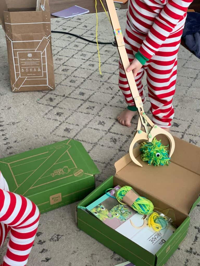 a child picking up a pom pom with a mechanical wooden claw from kiwico