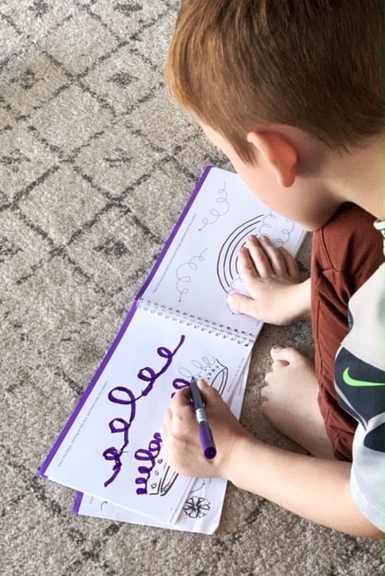 a kindergarten boy working on pre writing workbook tracing swirls and loops