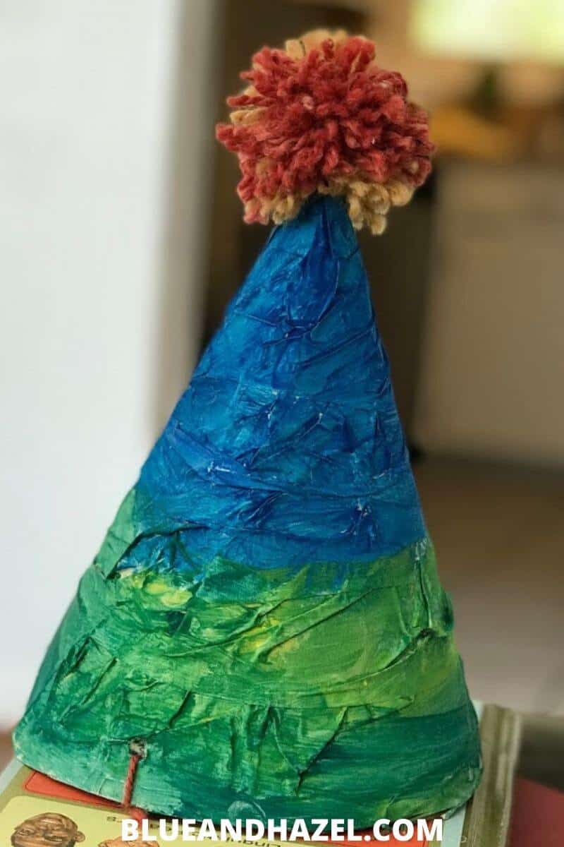 homemade birthday party hat painted blue and green, with an orange yarn ball on top