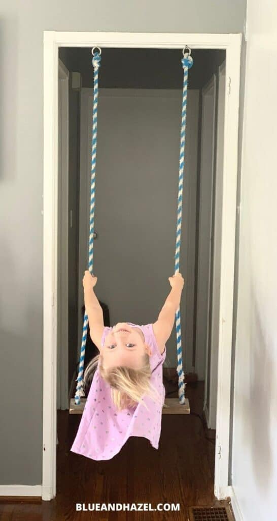 A little girl swinging on an indoor swing made of rope and a board.