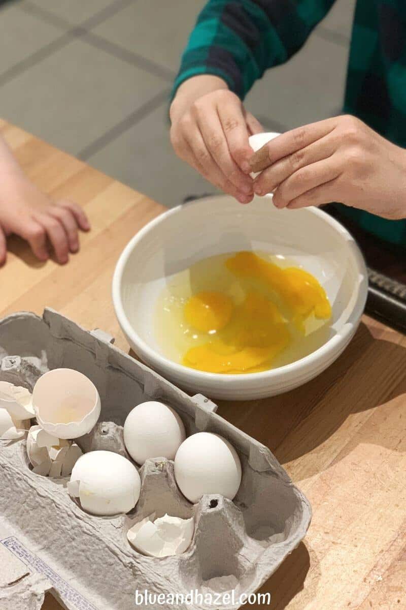 a 7 year old cracking eggs into a bowl learning life skills as part of his chores