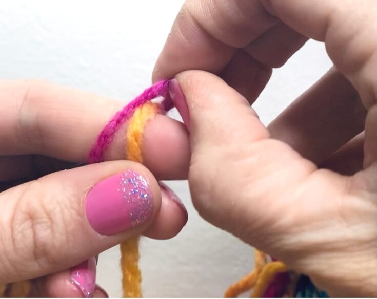 Fingers pulling a piece of yarn over while finger knitting.