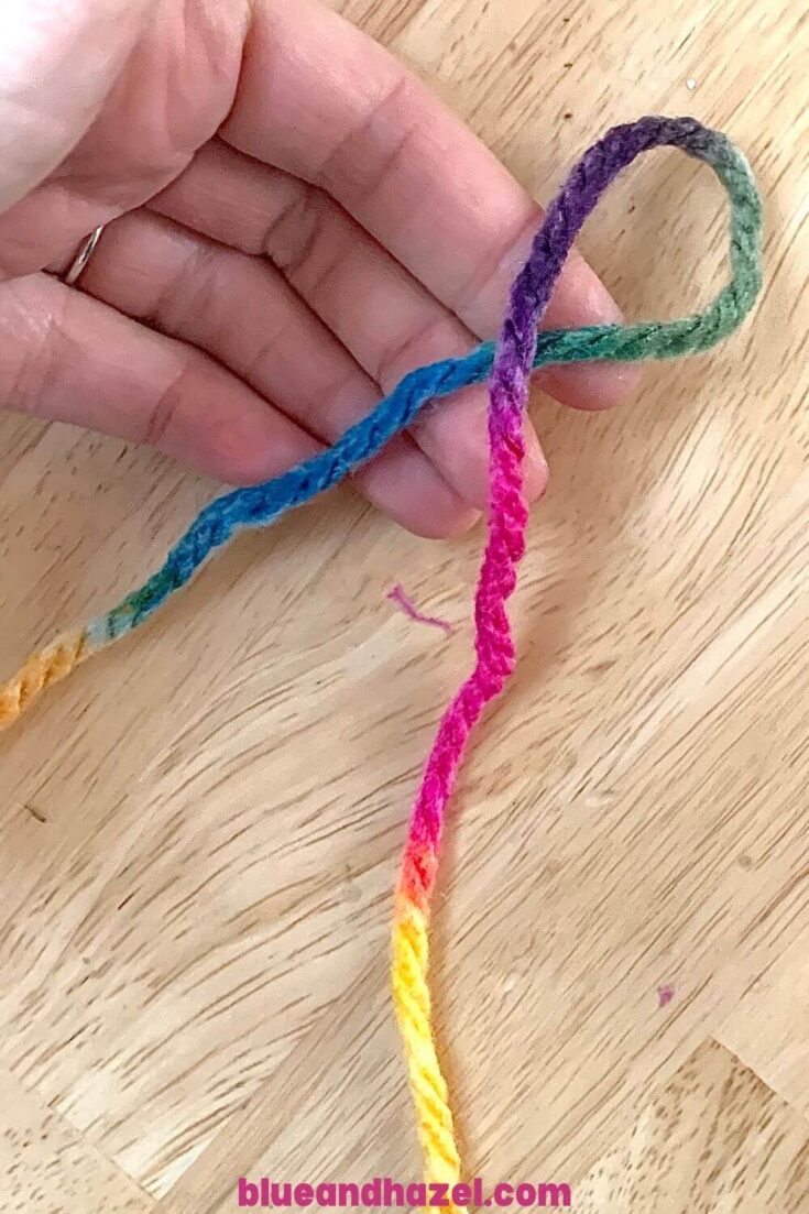 A piece of rainbow yarn looped over itself in preparation to do a slip knot for finger knitting. 