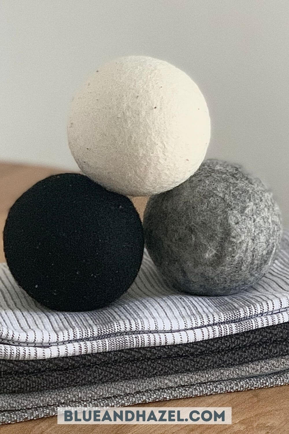 Set of 3 wool dryer balls from Dropps, including a black, white, and gray ball sitting on a stack of hand towels. 