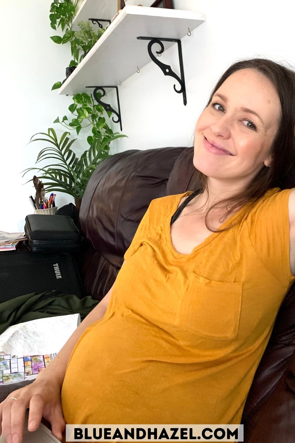 A pregnant mother sitting on her couch in a yellow t-shirt.