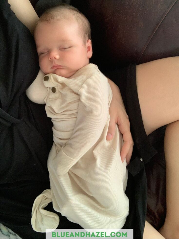 baby boy sleeping in his mother's arms in a cream colored newborn knotted onesie with hand mittens.
