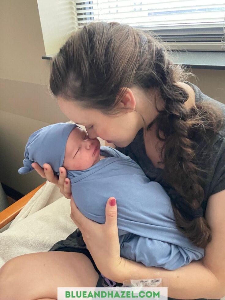 A mom snuggling her newborn at the hospital, wrapped in a blue swaddle and blue hat from Shop Quinn St.