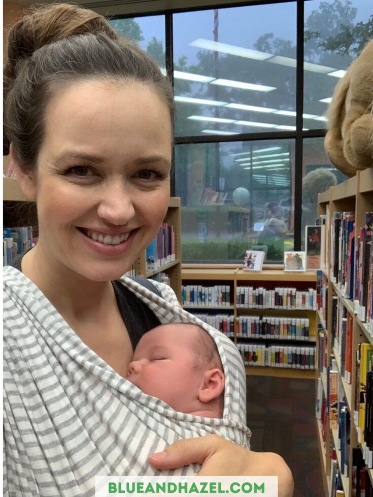 A newborn inside of a solly baby wrap sleeping on it's mother in a library.