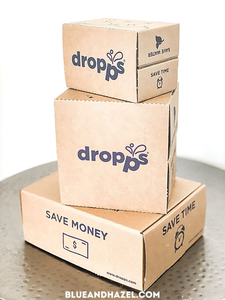 3 cardboard boxes of Dropps detergent pods delivered in the mail with packaging that says "save time" and "save money"