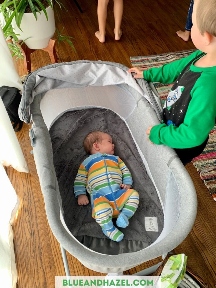 grey safety 1st bassinet with a newborn sleeping inside