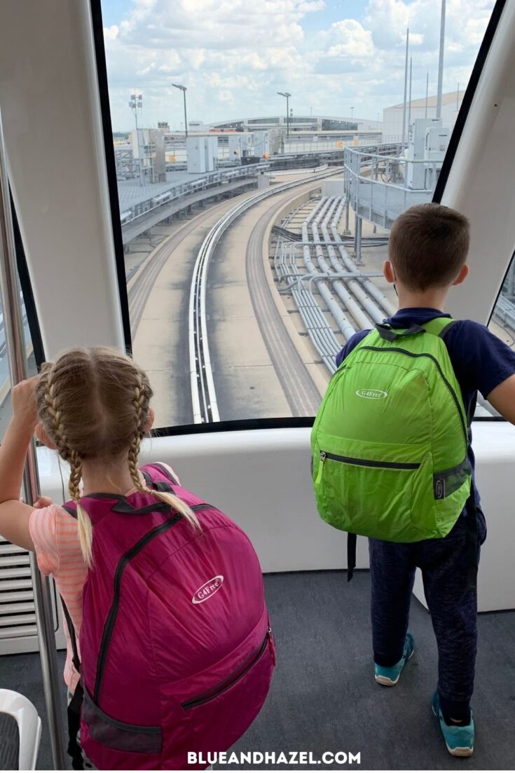 A boy and girl wearing a pink and green backpack on an airport train.