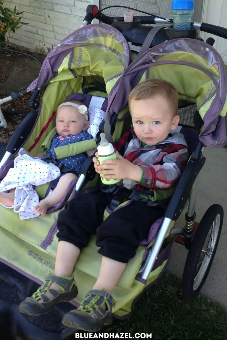 A toddler boy and his newborn sister riding in a green double jogging stroller.