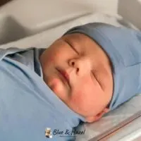 A newborn baby boy swaddled in blue and sleeping in a hospital bed