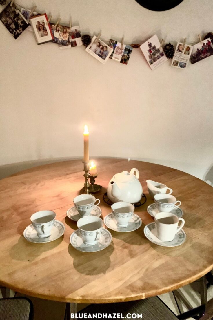 White tea cups and beeswax candles set out on a round wooden table for Christmas breakfast.