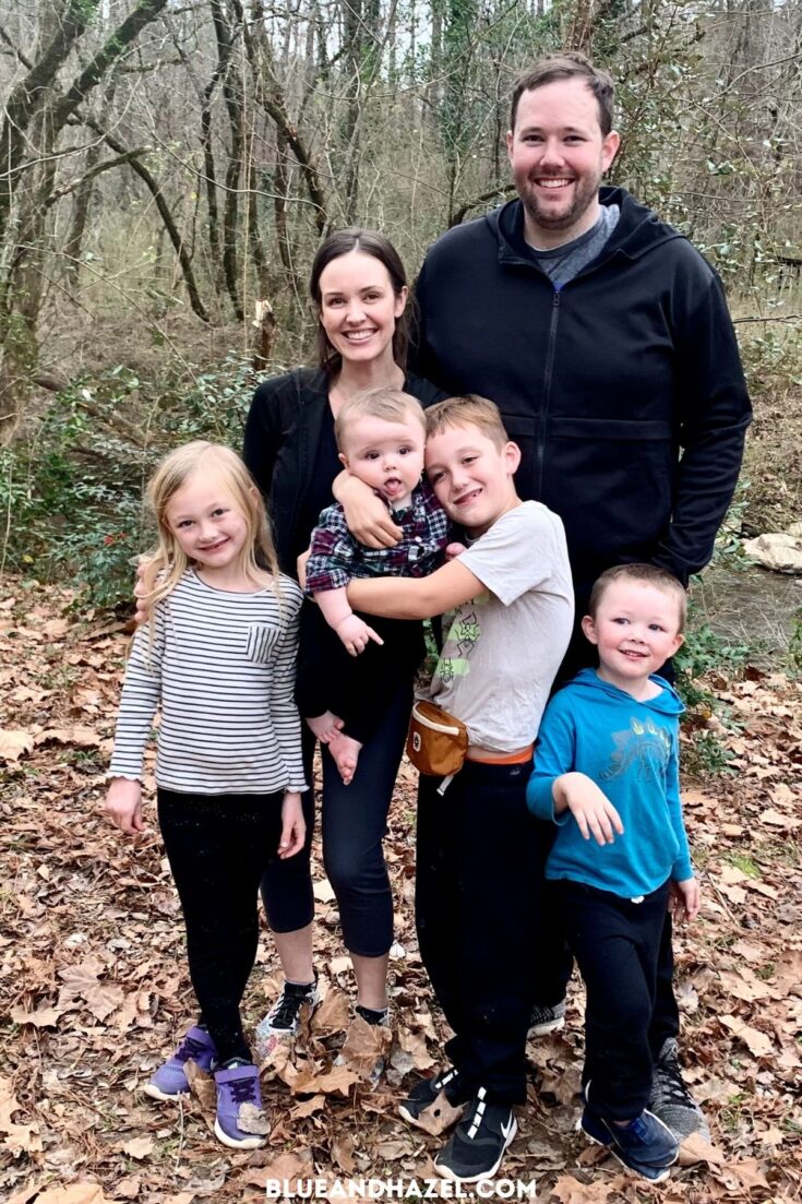 A family of 6 smiling for a photo in the woods on Christmas day. 